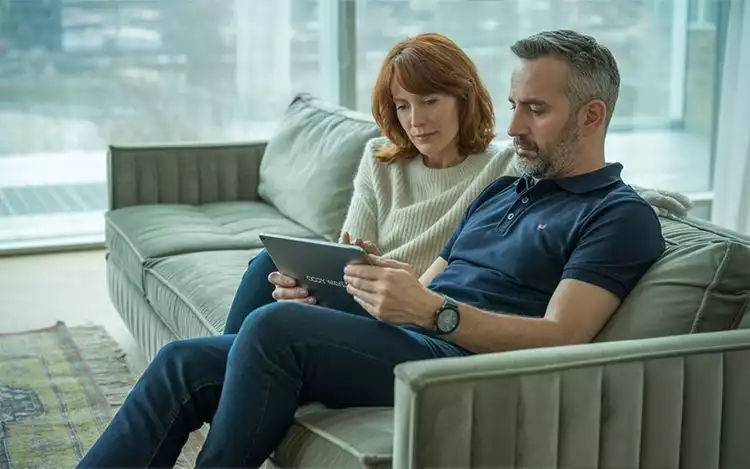 a man and a woman sitting on a couch looking at a tablet