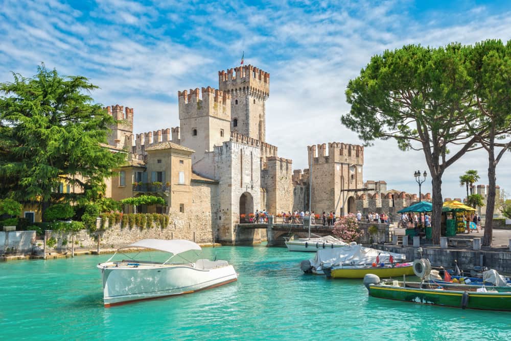 Scaligero castle surrounded by boats on the water, tourists and trees