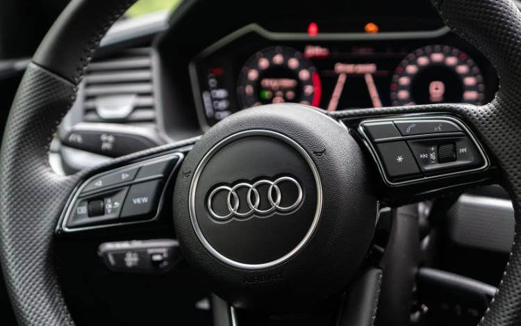 A black Audi steering wheel with the silver Audi logo featuring four rings in the centre.
