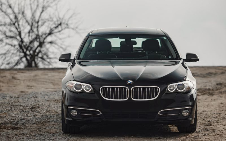  A black BMW parked on a dirt road with a bare tree on the left of the shot slightly out of focus
