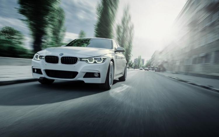 A white BMW driving quickly down a road with trees and buildings blurred behind it