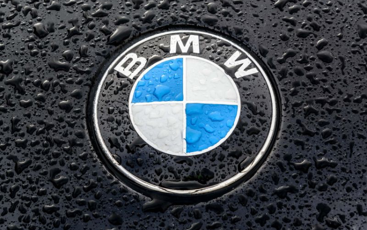 A close-up shot of the white and blue BMW logo on a black car covered in raindrops