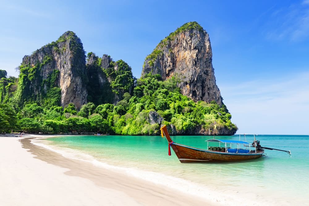 Thai traditional wooden longtail boat and beautiful sand on Railay Beach with trees and cliffs in the background