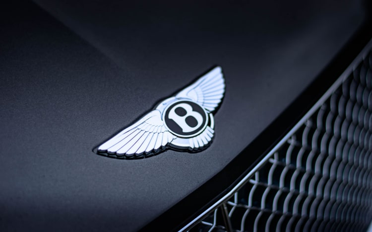 A close-up of a black Bentley only showing part of the grille and the Bentley emblem - a silver B with a pair of silver wings.