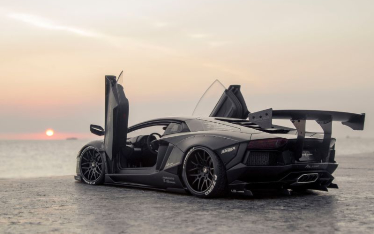 A black Lamborghini parked on a beach with its doors open and the sea and a pink sun visivle in the background