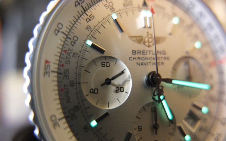 A close-up of a silver Breitling watch with a white outer rim and green lit-up hands