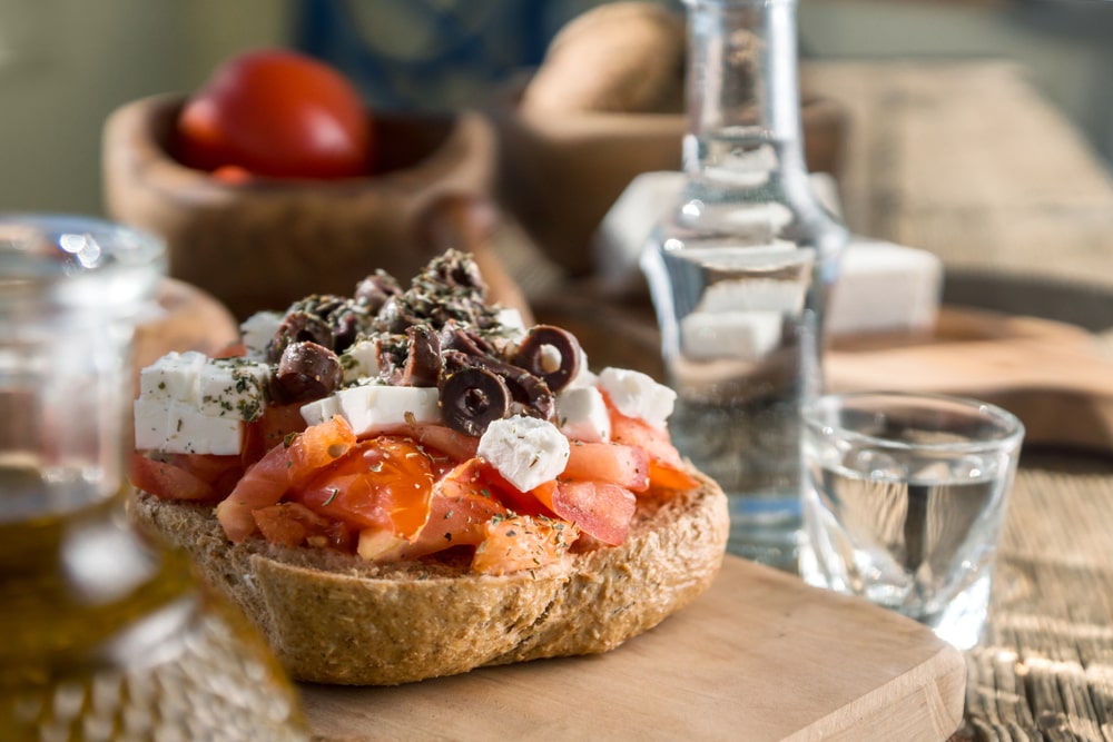 Dakos on a wood board with a glass of water beside it