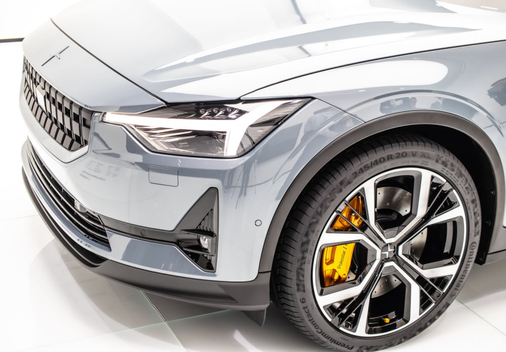 Close up shot of the side of a grey car bonnet featuring one tyre, grill and front light. Presented in a show room with gleaming white light bouncing off it.