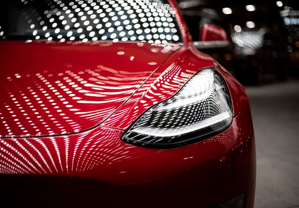 Front shot of the side of a shiny red sports car featuring the right light. The car has dotted white lights all over the bonnet and window screen and has been taken in a dimly lit garage.