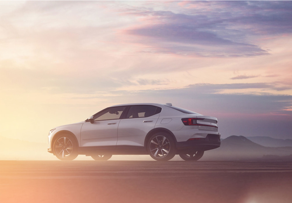 White luxury 4x4 parked in a dusty mountain valley, with ominous mountainscapes in the background set against a pink, purple and orange skyline at dawn.