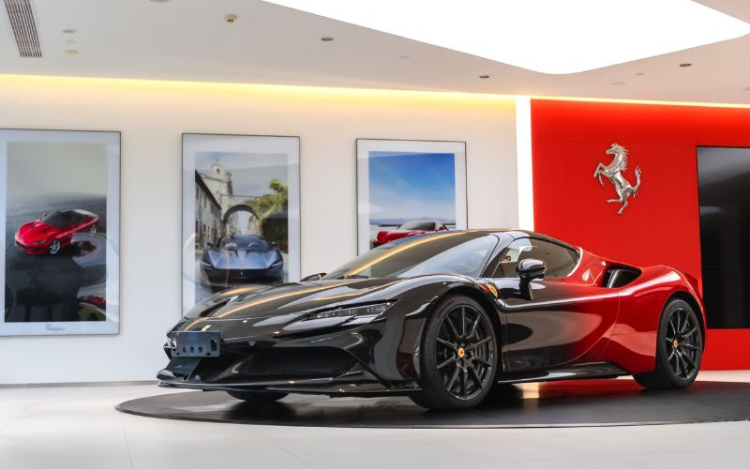 A shiny black and red Ferrari on a round black platform in a car showroom. There are 3 framed Ferrari images on the white walls behind it and a silver horse logo on a red wall on the right
