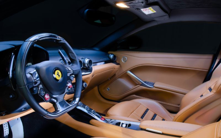 The inside of a Ferrari with a black steering wheel featuring a yellow logo and brown leather seats