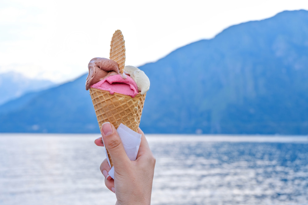 Someone holding an ice cream cone with pink, white and brown scoops and a view of Lake Como landscape blurred in the background
