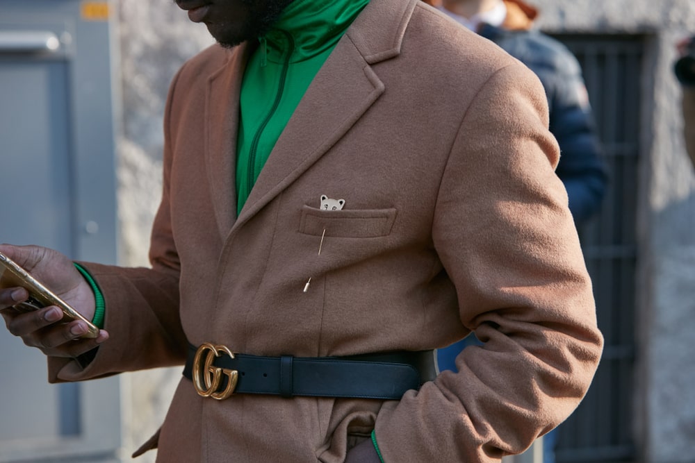 Person looking at their phone while wearing a light brown suit, a green shirt and a Gucci belt