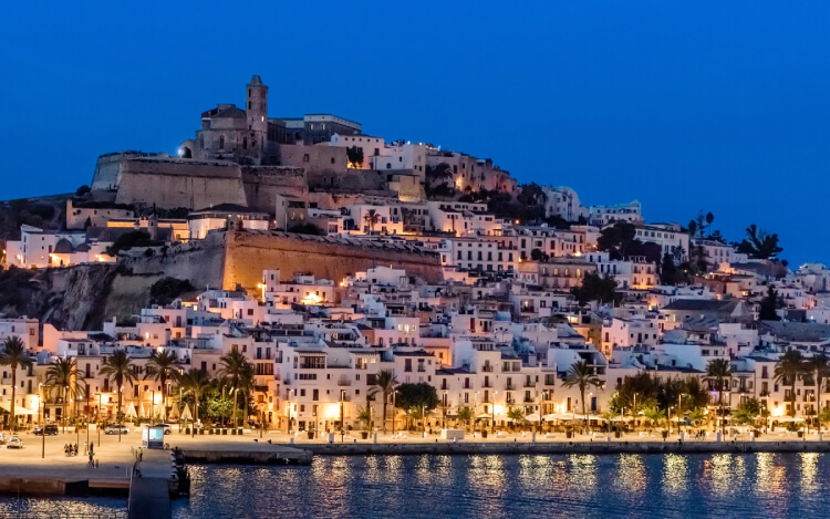 Night view in Ibiza illuminated by dazzling lights and the glow of the moonlit sea.