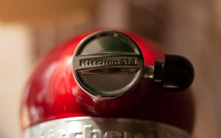 a close-up image of a red KitchenAid stand mixer with a silver stamped logo and black component.