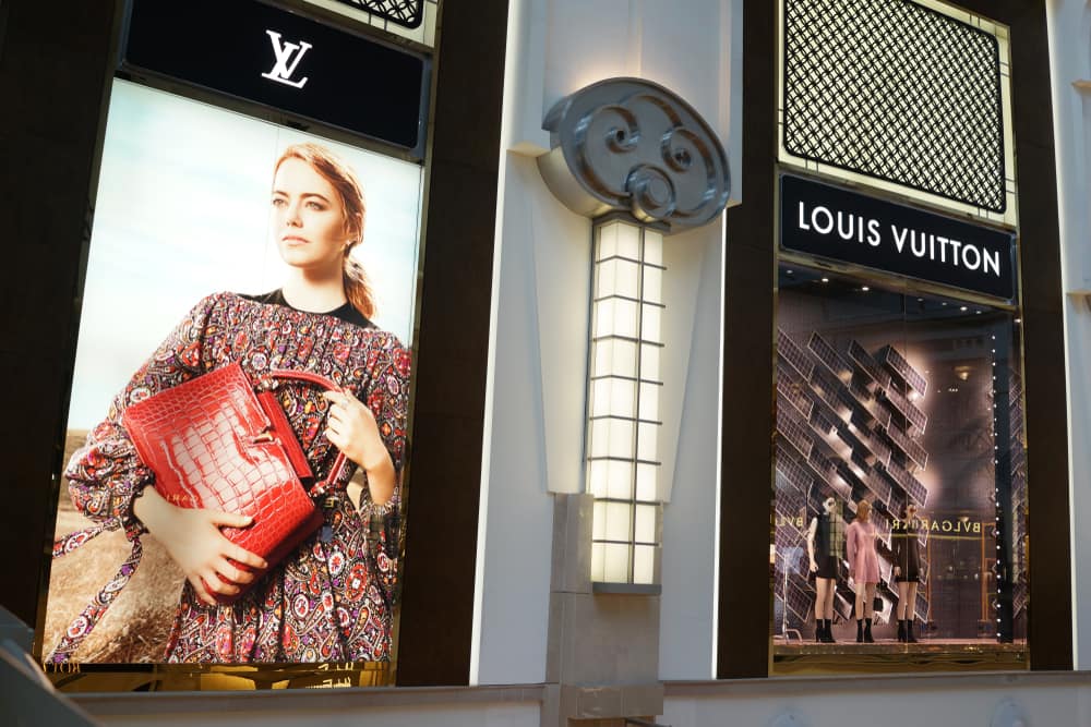 Louis Vuitton shop front with mannequins display on the right and a big poster of actress Emma Stone on the left