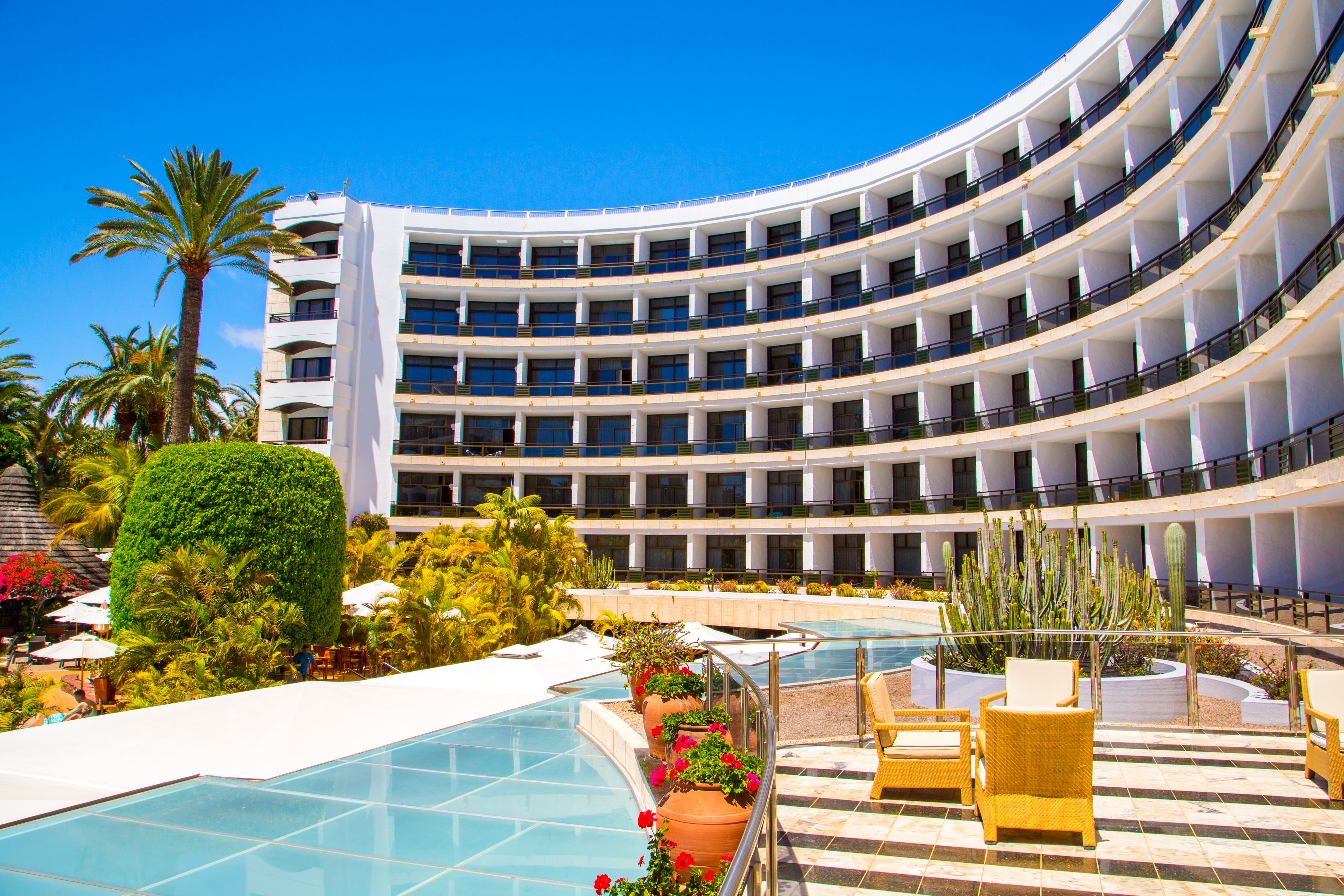 Luxury six-story white hotel in Spain overlooking an infinity pool with a stone seating area.