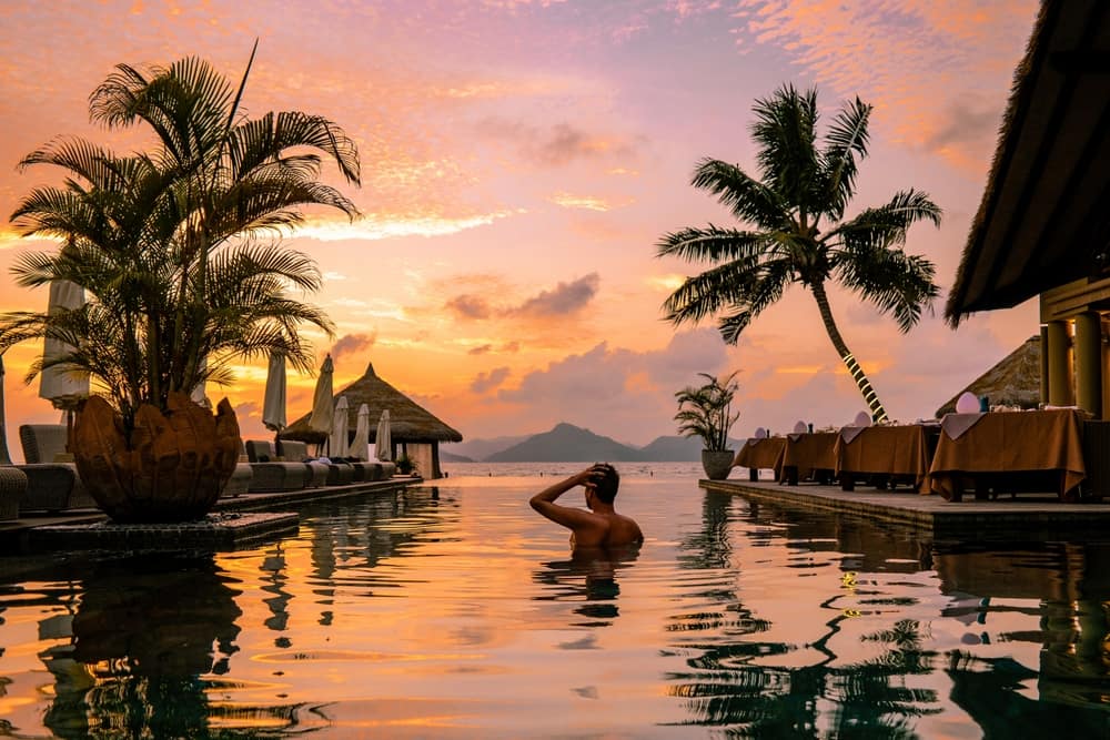 Person relaxing in a luxury resort swimming pool at sunset