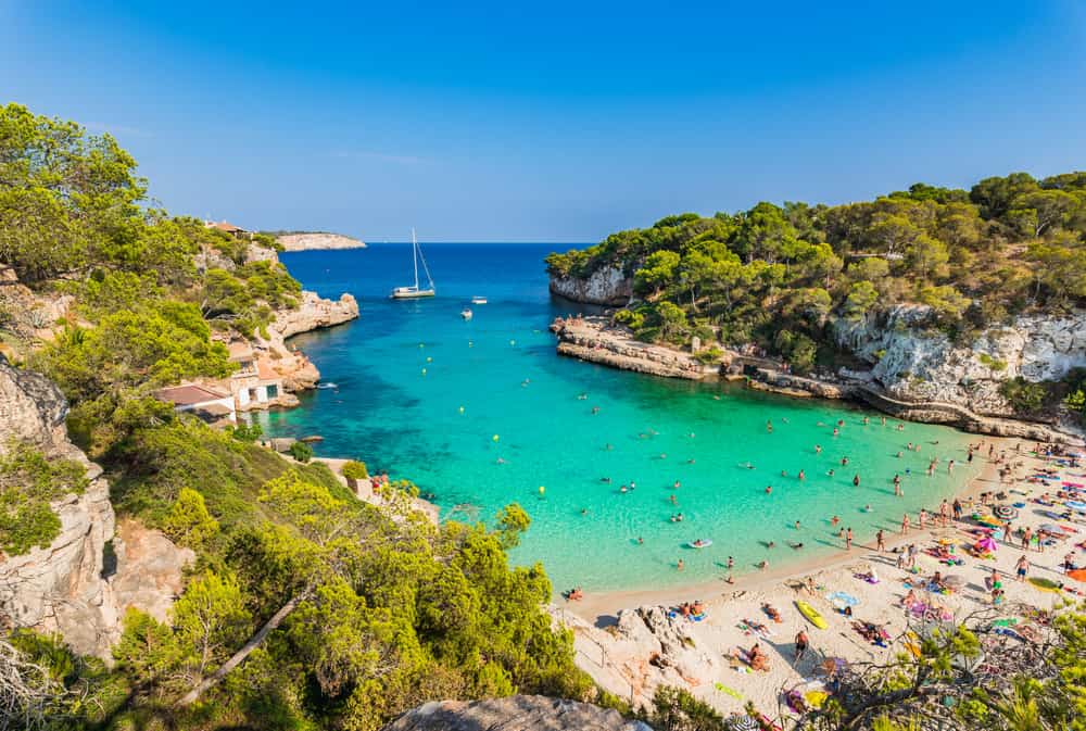 People hanging out at Cala Llombards beach with turquoise water and cliffs at either side