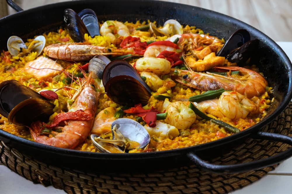 Close-up shot of a Paella dish with mussels, amandi and prawns on a pillow of rice in a black pan