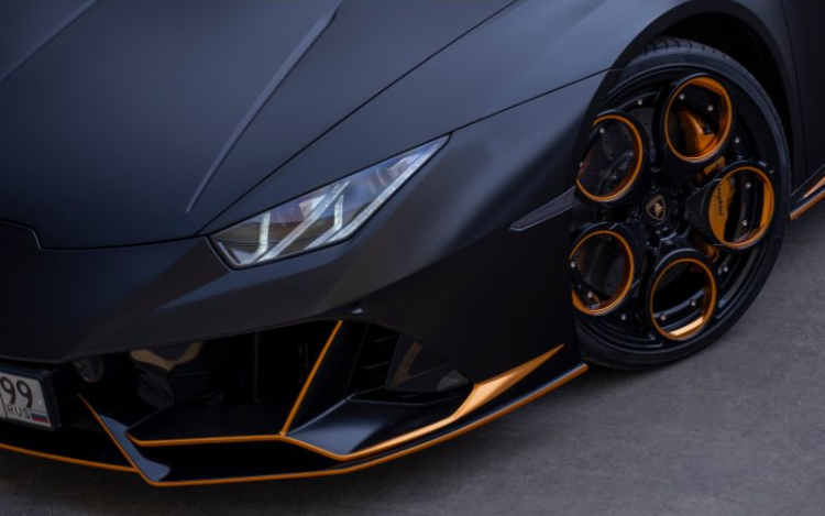 A matte black Lamborghini with gold trim detailing on the wheels and the front of the car. The license plate is partially visible with the numbers 99