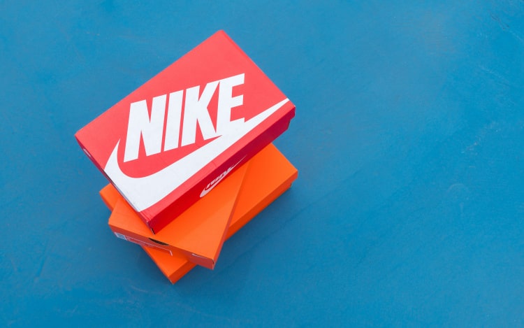 Two orange shoes boxes with a pink shoe box stacked on top of them, the pink box has a white swoosh on it and reads the word NIKE in a diagonal pattern.