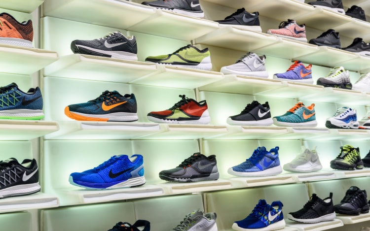 30 pairs of Nike trainers photographed across five shelves in a shop display unit with white light against them. All the trainers are different colours