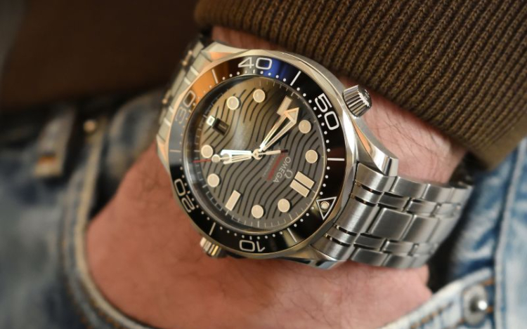 A silver Omega watch on a man’s arm with wavy detailing on the face and a black outer rim.