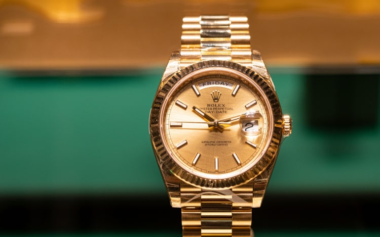 A gold Rolex watch in front of a gold and green background