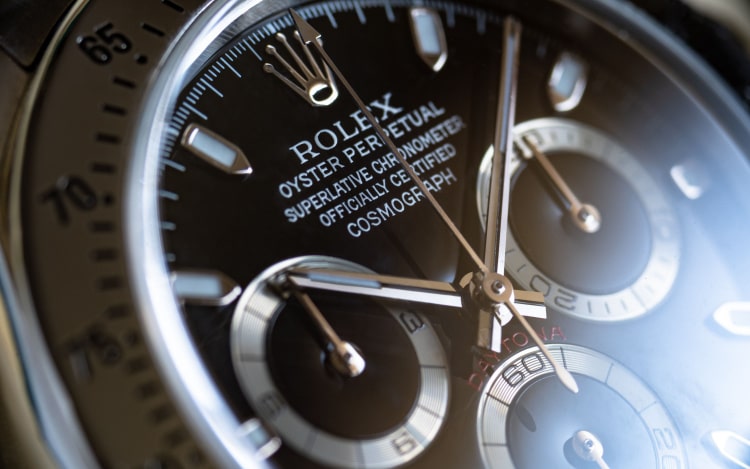 A close-up image of a Rolex. The gold Rolex logo of a crown is visible along with the brand name in white, part of a gold dial and gold hands