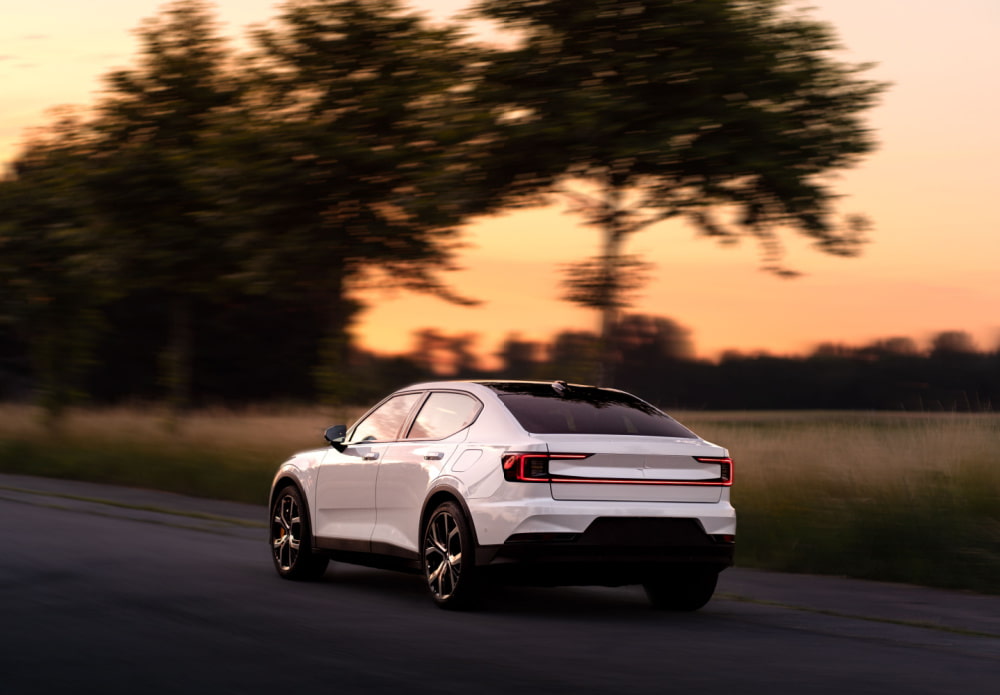 Luxury white 4x4 shot in motion on an empty country road with a orange and yellow sunset in the background, nestled amongst trees.