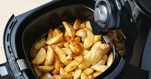 Black air fryer drawer open and full of crispy potato wedges.