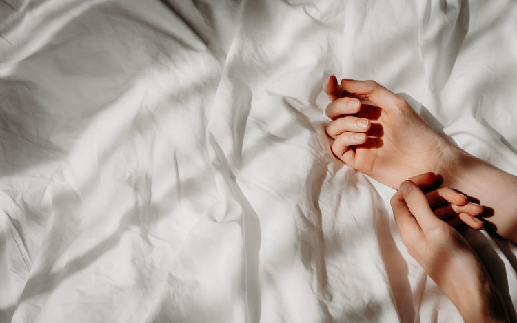 A pair of white hands resting on a white duvet cover in the daytime