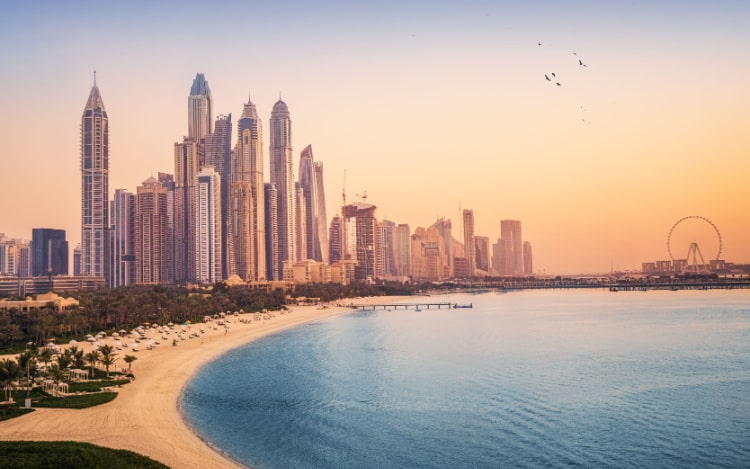 A beach in Abu Dhabi with several skyscrapers and a ferris wheel in the background.