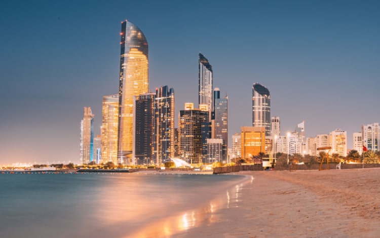 A beach in Abu Dhabi with several illuminated skyscrapers along the shore.