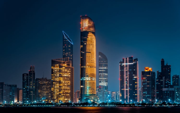 Abu Dhabi’s city skyline at night, showing several illuminated skyscrapers against a clear night sky.