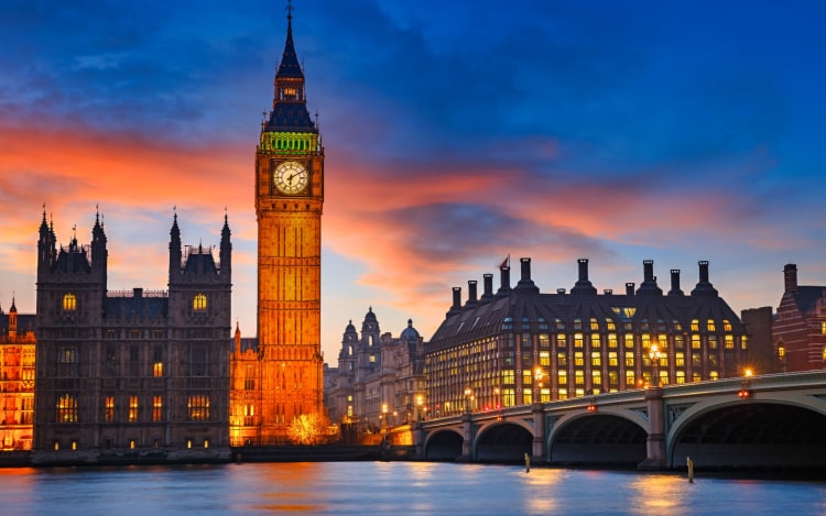 A view of Big Ben and the houses of Parliament at dusk over the river. The sky is dark blue with some pink clouds.