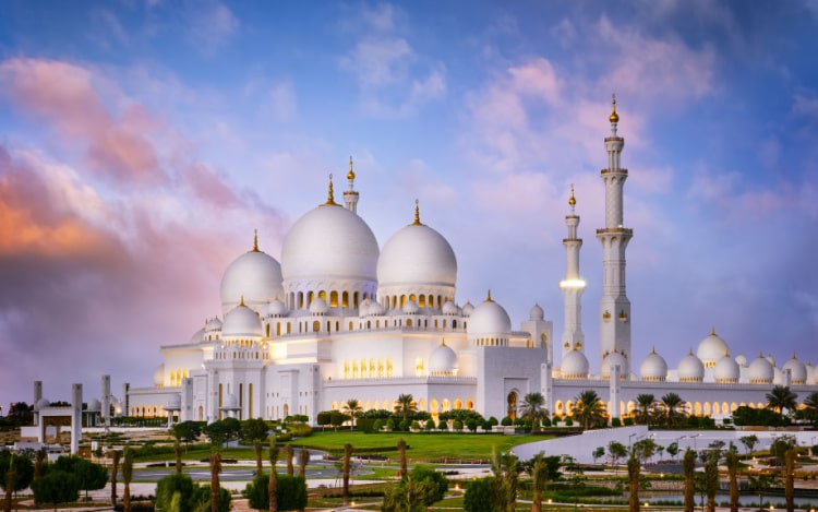 The Sheikh Zayed Grand Mosque, a large white domed building, under a blue sky with pink clouds.