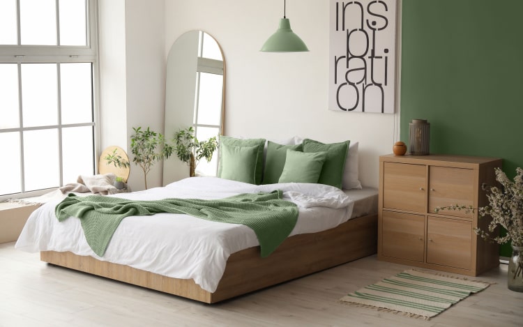 A bedroom with a green and white colour scheme. The pillows, throw, lamp, and right-hand side of the wall are green.