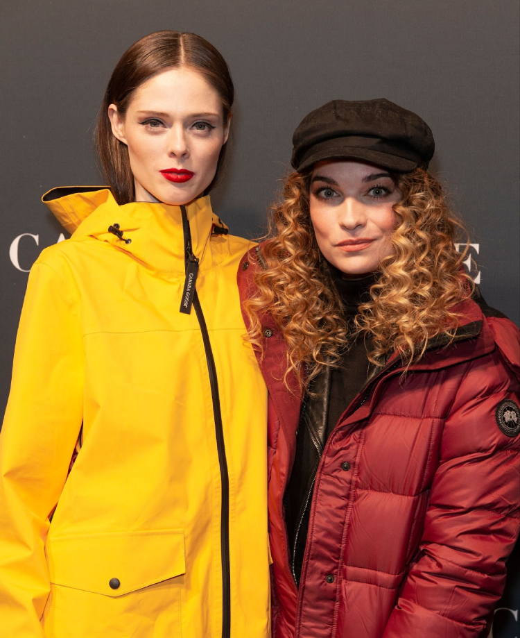 two female celebrities at a red carpet event are wearing Canada Goose coats and smiling for the camera