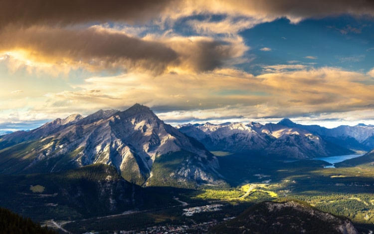 The mountains of Banff are slightly snowy under a partially sunny sky, with some orange clouds above the mountaintops.