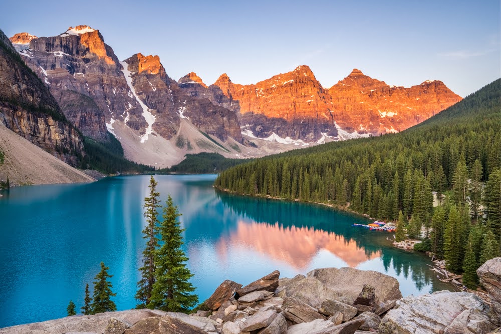 Sunrise over Moraine Lake with trees on the right and rocky mountains in the background