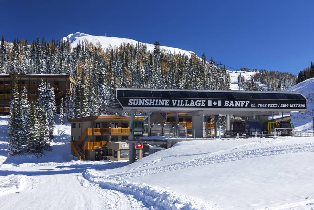 Lodges and chairlift entrance surrounded by snow with tall trees in the background