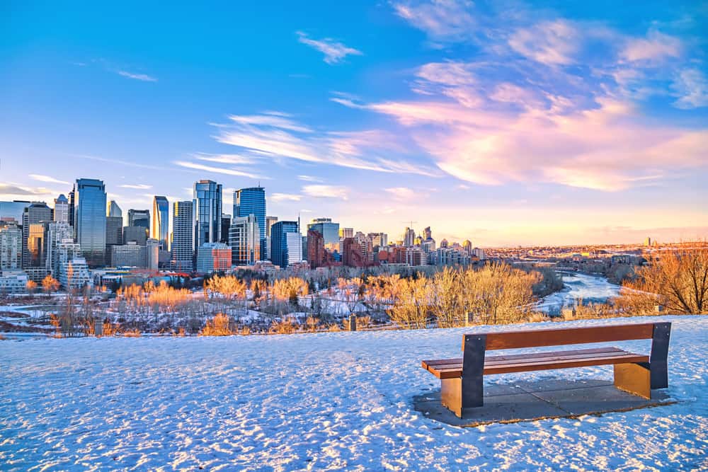 A bench on a snowy hill looking towards downtown Calgary with a warm sunrise
