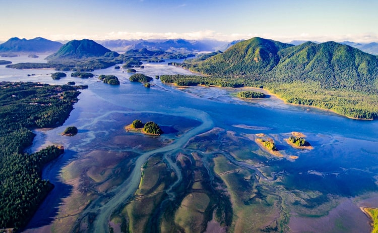 Aerial image of a Sound. The water is deep shades of blue with purple and green. There are small green islands dotted on the water and a larger, mountainous island on the right