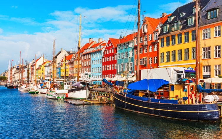 A row of colourful Copenhagen houses on the shore on a clear day, with multiple stationary boats outside.