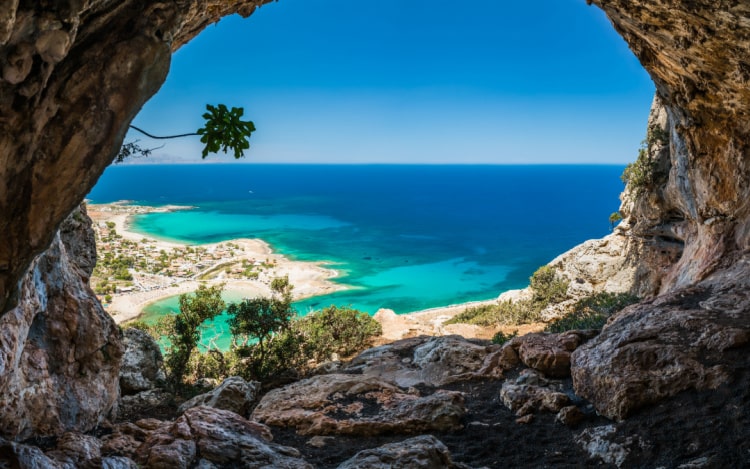 A photo taken from the inside of a cave in Crete, looking out to the sea and beach below.