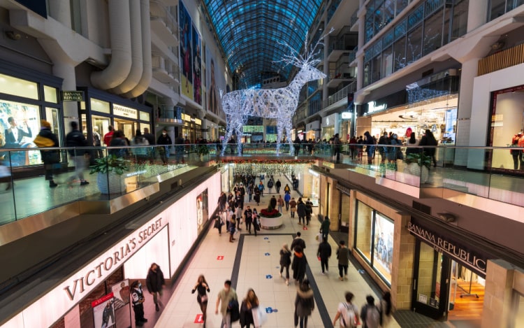 Toronto’s Eaton Centre shopping mall around Christmas time, with several shoppers passing by on two levels and a large reindeer decoration in the centre.