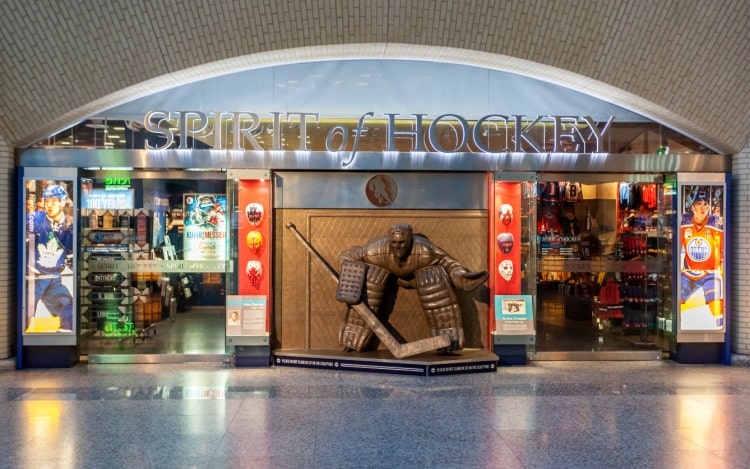 A gift shop in Toronto’s Hockey Hall of Fame, with a bronze statue of a goalie, shop windows with merchandise, and the words ‘Spirit of Hockey’ above the store.